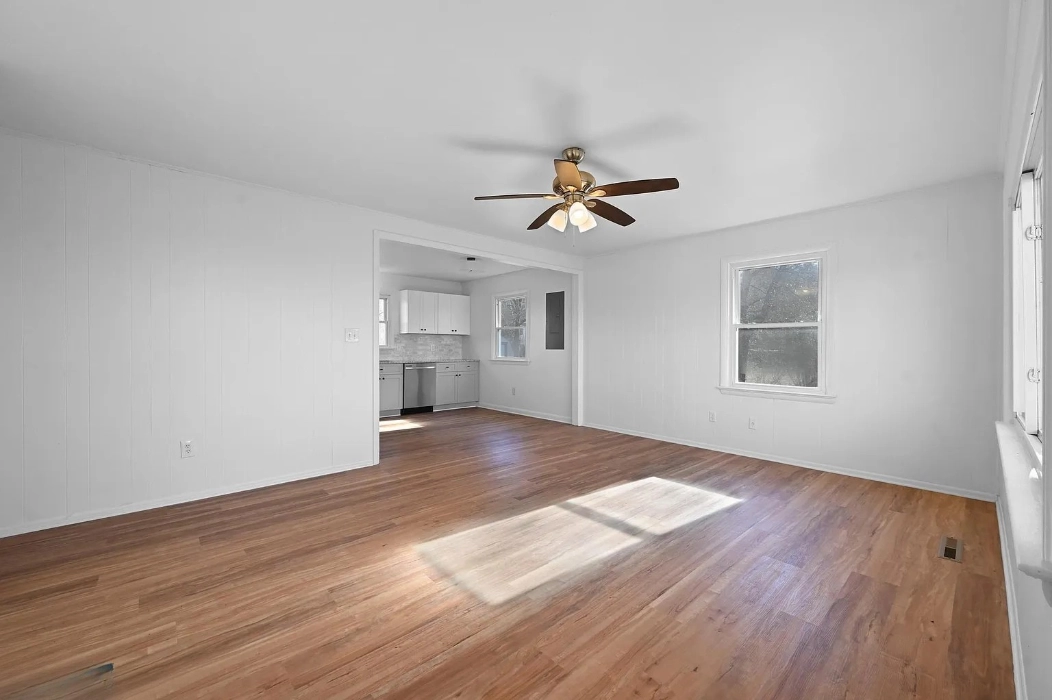 Bright and renovated living room with fresh white walls, wood flooring, and a ceiling fan, showcasing a clean and modern update after purchasing the home quickly directly from the seller